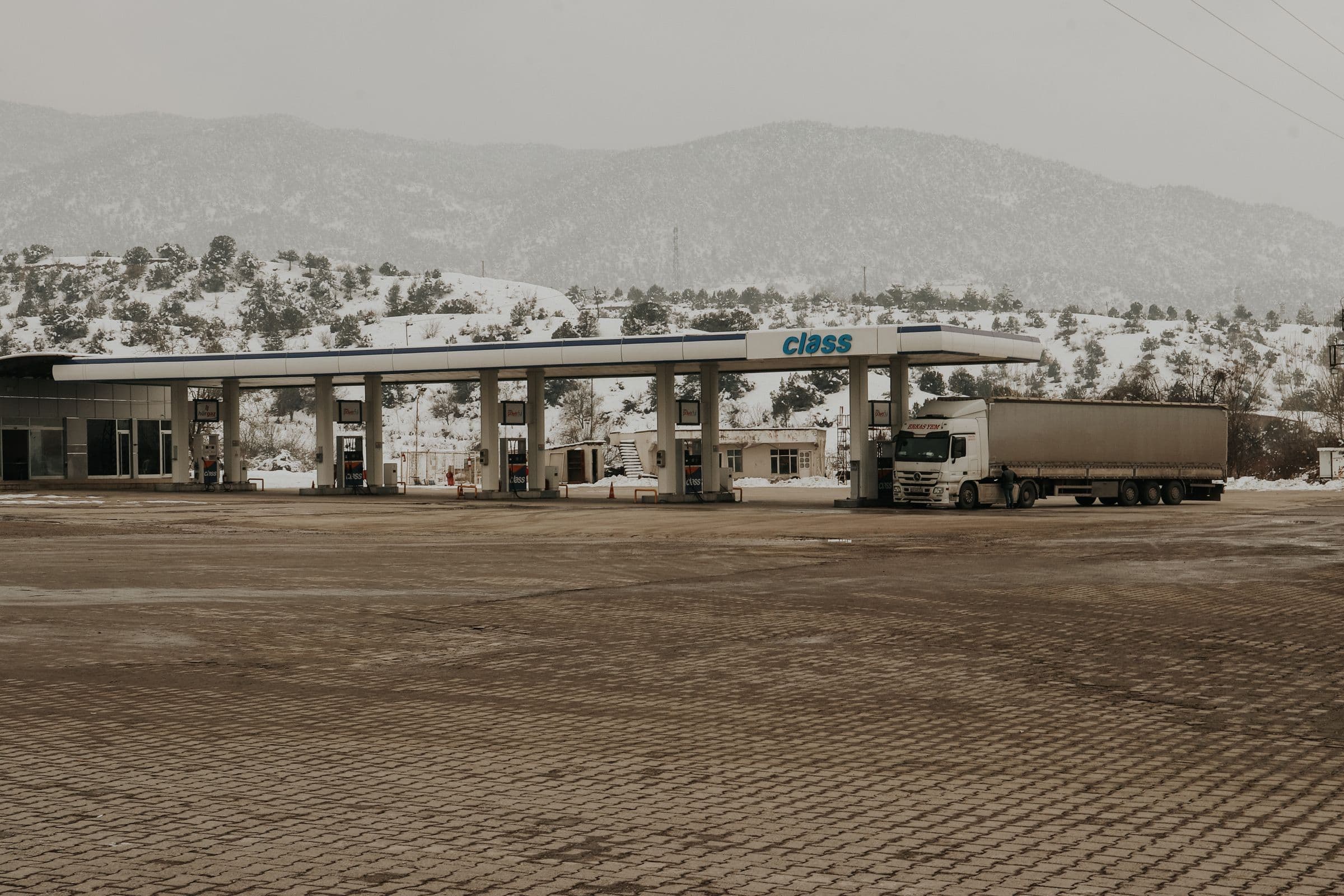 Camion articulat la o stație de alimentare, cu munți înzăpeziți în fundal